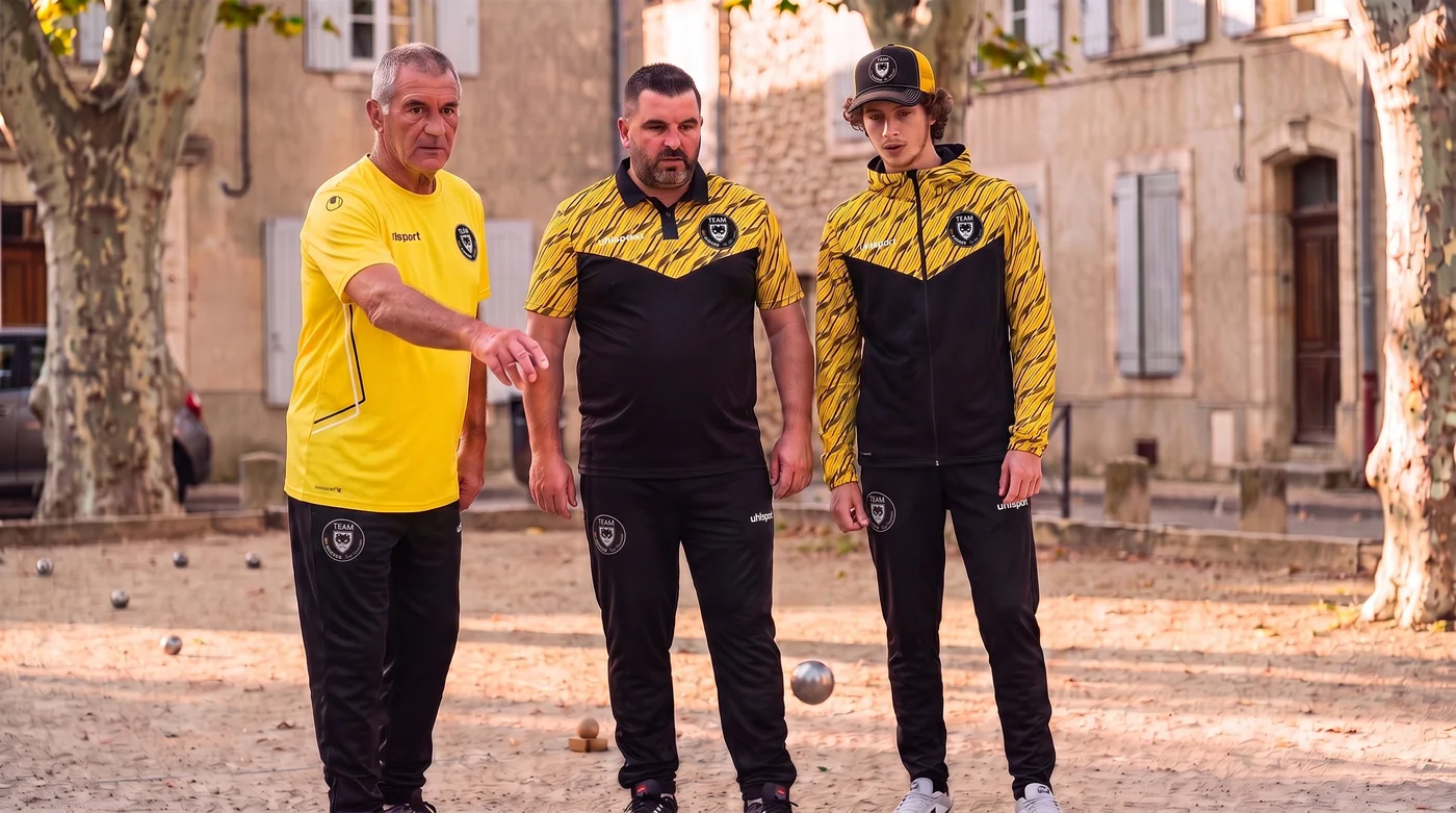 Trois joueurs de la Team MPpronos en maillot Equipe 29, polo Progressive, veste à capuche et casquette trucker sur un boulodrome de village